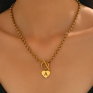 Gros plan du collier doré avec pendentif cœur lettre A et fermoir OT sur le cou
