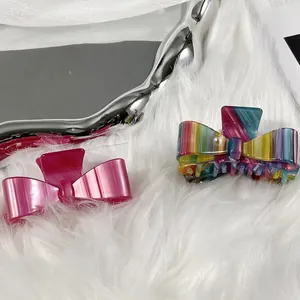 Elegant acetate bow hair claws in marble pink and rainbow stripes on a silver tray