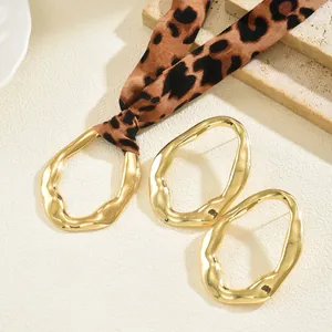 Golden irregular wavy metal earrings with leopard print silk scarf on a stone background
