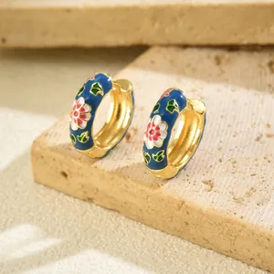 Detailed close-up of gold-plated hoop earrings with blue enamel and floral patterns