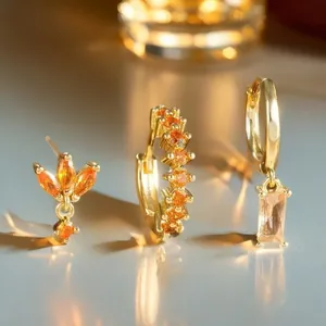 Macro detail of gold-plated geometric earrings set with sparkling orange zircon stones