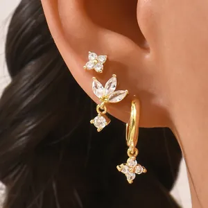 Close-up of three gold geometric stud earrings with zircons on a female model ear
