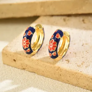 Detailed view of navy blue enamel hoop earrings with red floral patterns on a stone base