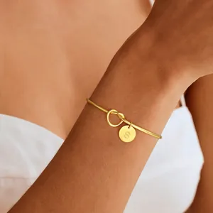 Adjustable golden bangle featuring a knot design and round initial S pendant on wrist
