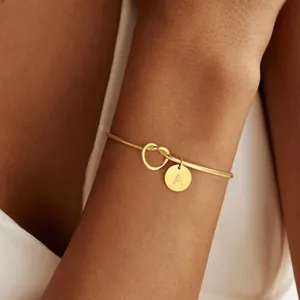 Detailed shot of a gold knotted bracelet with a round initial A charm on a model's wrist