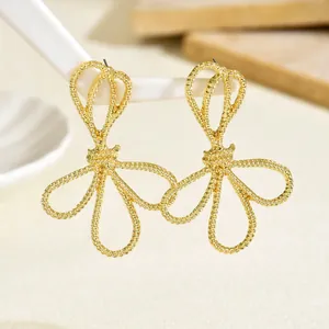 Detailed close-up of golden spiral bow earrings hanging on a white geometric stand