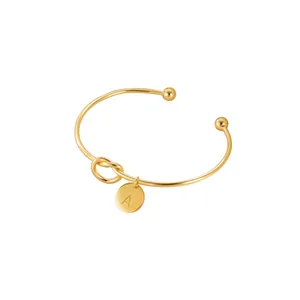 Adjustable gold open bangle featuring a knot design and a round letter A charm