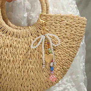 Handmade pearl bow keychain with golden heart and colorful beads on straw bag