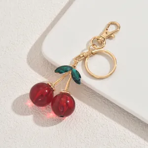 Cute red cherry keychain with gold metal stem and green gemstone leaves on white background