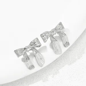 Macro detail of silver ribbon earrings with textured metallic pleats on marble surface
