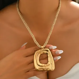 Detailed close-up of a large textured gold abstract pendant with a twisted rope chain