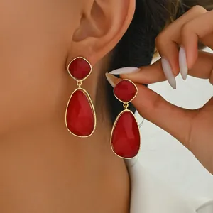 Close-up of red teardrop-shaped gemstone earrings with gold-tone geometric metal frames