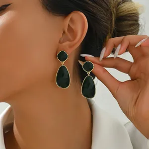 Close-up of geometric green faceted drop earrings with gold frames on a model