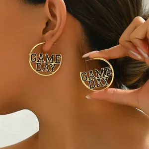 Detail shot of gold-plated hoop earrings with black enamel GAME DAY lettering