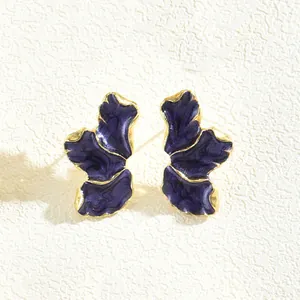Macro orecchini a quadrifoglio viola scuro con bordi dorati su superficie bianca