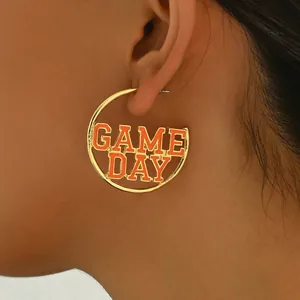 Golden hoop earrings with orange Game Day lettering worn by a model in a close-up view