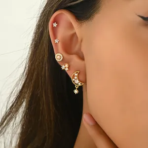 Detailopname van gouden ster- en maan-oorstekers met zirkonia steentjes op het oor