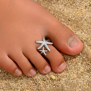 Detailed macro view of adjustable silver starfish toe rings on beach sand background
