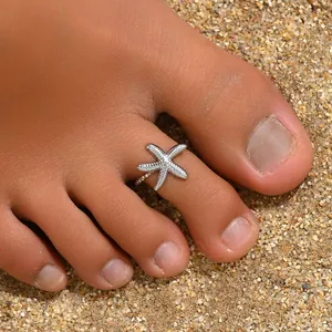 Macro shot of silver starfish toe ring with textured surface on a sandy beach