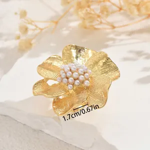 Golden geometric flower open ring with white pearls on a textured stone surface