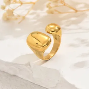 Anillo abierto dorado irregular con diseño esférico brillante sobre superficie blanca