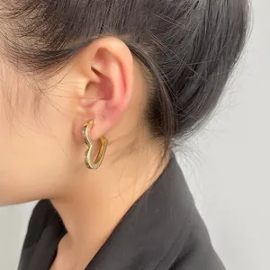 Primo piano di una modella che indossa un orecchino a cuore dorato lucido stile minimalista
