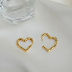 Primo piano di orecchini a cerchio a cuore dorati con finitura lucida su seta beige