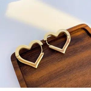 Eleganti orecchini a cerchio a forma di cuore dorati su vassoio in legno scuro