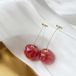 Detalle de pendientes de cereza en resina transparente y pétalos de flores secas