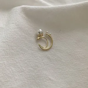 Detail of golden double C-ring ear cuff with large and small pearls on white fabric