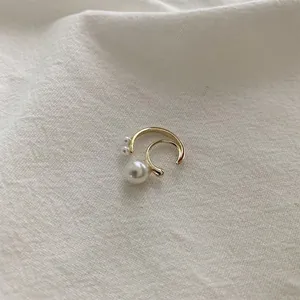 Macro detail of minimalist gold ear cuff with three white pearls on white fabric background