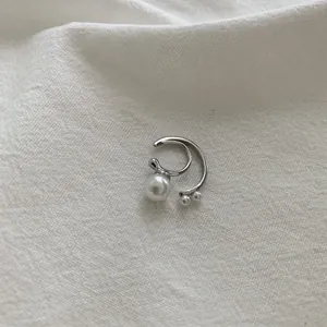 Detail of silver double C-shaped ear cuff with white pearls on a textured white fabric