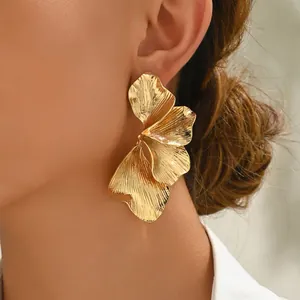 Orecchini a petalo dorati a strati con texture metallica spazzolata indossati da modella