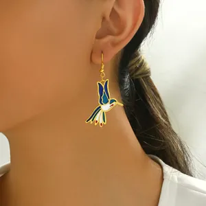 Close-up of a colorful hummingbird earring featuring blue and red enamel on a gold base