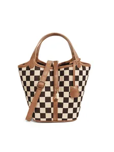 Détail du sac seau à damier avec poignées en cuir et serrure dorée sur fond blanc