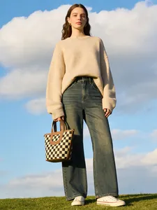Model met een dambord emmertas, een gebreide trui en een spijkerbroek op het gras