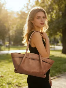 Brown leather oversized tote bag with metal buckle detail shown in warm outdoor sunlight