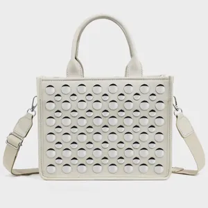 Detailed view of beige PU tote bag featuring rows of silver round metal rivets and strap
