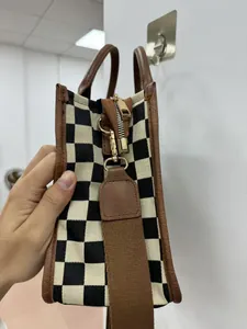 Detailed close-up of checkerboard tote bag with brown leather trim and golden metal zipper