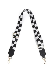 Detail of checkered canvas bag strap with gold metal lobster claws and black leather ends