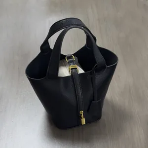 Close-up of black litchi grain leather tote with golden padlock and canvas inner pouch