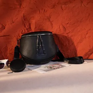 Detail der schwarzen Umhängetasche aus genarbtem Leder mit Gurt und kleiner Rundtasche