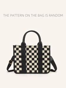 Detail of checkered straw tote bag featuring black handles and adjustable shoulder strap