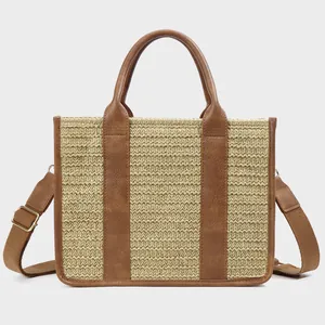 Detail of woven straw tote bag featuring brown leather trim and adjustable canvas strap