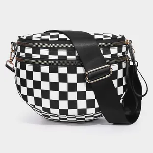 Detail view of denim checkerboard bag showing dual gold zippers and wide nylon strap
