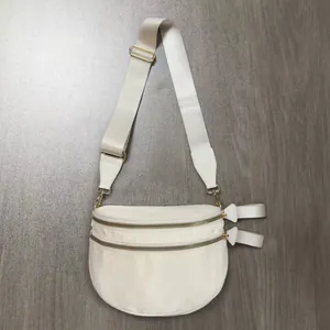 Close-up of beige nylon crossbody bag with double gold zippers and wide woven strap