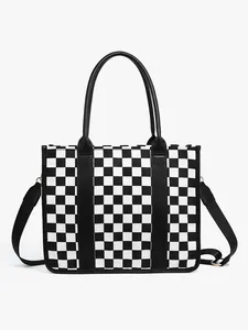 Detail of checkered straw tote bag with black leather handles and crossbody strap