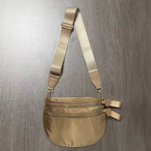 Detail of tan checkerboard crossbody bag with three golden zippers and wide nylon strap
