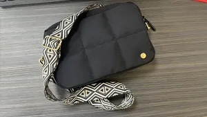 Detail of black quilted crossbody bag with patterned wide strap on a dark surface