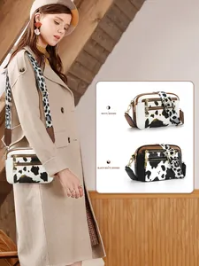 Detail view of cow print crossbody bag with dual zipper pockets and wide fabric strap